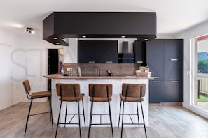 A modern kitchen with a central island, bar stools, and dark cabinetry. - Le Cappatti, 2 bedroom apartment (Nice)