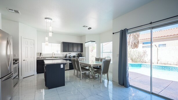 A modern kitchen with a central island, a dining area with a glass table, and a view of a swimming pool through large sliding doors. - Gorgeous 5-bedroom house with Pool in North Las Vegas (North Las Vegas)
