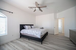 Ein Schlafzimmer mit Bett, Deckenventilator, Kommode und Tür zu einem anderen Raum.