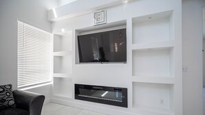 A modern living room with a flat-screen TV mounted on a white wall, a black leather sofa, and a patterned throw pillow. - Gorgeous 5-bedroom house with Pool in North Las Vegas (North Las Vegas)