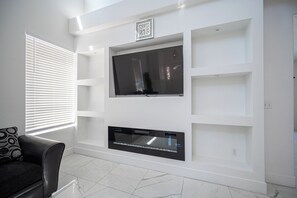 A modern living room with a flat-screen TV mounted on a white wall, a black leather sofa, and a patterned throw pillow. - Gorgeous 5-bedroom house with Pool in North Las Vegas (North Las Vegas)