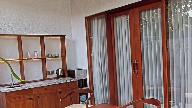 A compact kitchen with a built-in shelf, a sink, and a toaster. There are two wooden chairs with cushions. - Cozy 1-bedroom hotel suite in enchanting Ubud
with AC (Gianyar)