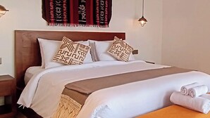 A neatly made bed with patterned pillows, a headboard, and a bedside table with a lamp. - Cozy 1-bedroom hotel suite in enchanting Ubud
with AC (Gianyar)