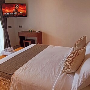 A hotel room with a bed, a desk, a television displaying a movie, and a window with curtains. - Cozy 1-bedroom hotel suite in enchanting Ubud
with AC (Gianyar)