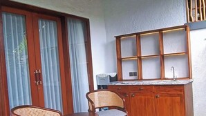 Kompakti keittiö, jossa on puiset kaapit, sisäänrakennettu pesuallas ja pieni ruokailutila, jossa on kaksi tuolia.