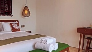 Hotellihuone, jossa on sänky, penkki pyyhkeineen, työpöytä ja riippuvalaisin.