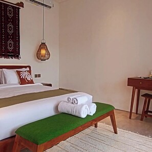 Ein Hotelzimmer mit Bett, einer Sitzbank mit Handtüchern, einem Schreibtisch und einer Pendelleuchte.