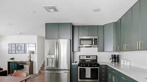 A modern kitchen with stainless steel appliances, teal cabinetry, and a white countertop.
