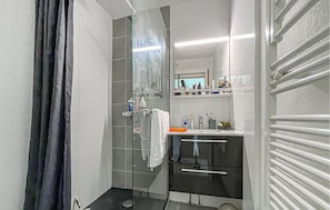 Ein modernes Badezimmer mit einer Duschkabine aus Glas, einem weißen Waschbecken und einem Spiegel über der Ablagefläche.