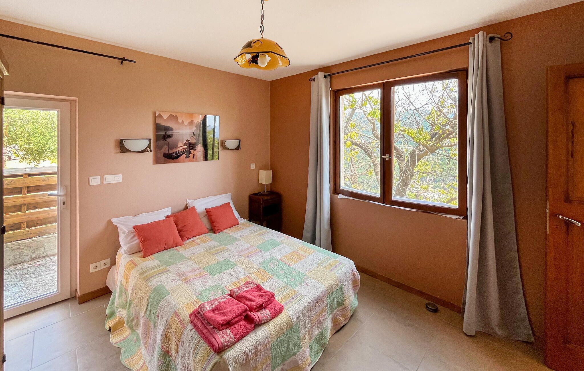 Un dormitorio con cama, ventana con cortinas, un cuadro en la pared y una puerta.