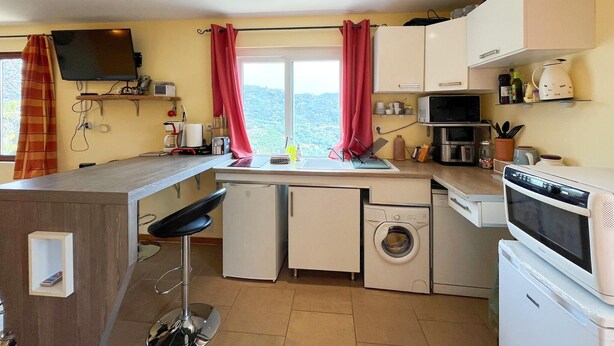 A compact kitchen with a washing machine, microwave, and a bar stool. - Lovely home in Châteauneuf-Villevieil (Châteauneuf-Villevieil)