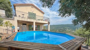A swimming pool with a wooden deck, a two-story building with a balcony, and a view of the countryside. - Lovely home in Châteauneuf-Villevieil (Châteauneuf-Villevieil)
