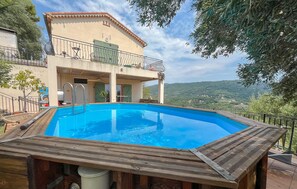 A swimming pool with a wooden deck, a two-story building with a balcony, and a view of the countryside. - Lovely home in Châteauneuf-Villevieil (Châteauneuf-Villevieil)