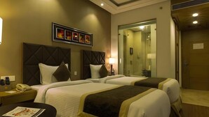 Une chambre d’hôtel avec deux lits, une table de chevet avec une lampe et une douche séparée par des parois en verre.