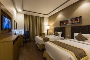A hotel room with two beds, a desk, a TV, and a window with curtains. - The Grand Jbr (Lucknow)