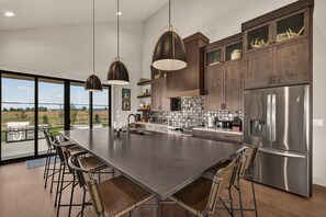 A modern kitchen with a large island, stainless steel appliances, and a view to the outdoors. - Teton Sunset 3BR luxury home sleeps 12 with private hot tub & unbeatable Teton mtn views. (Driggs)