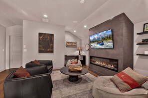 Un salon moderne doté d’une cheminée, d’un téléviseur fixé au mur et d’un coin salon confortable.