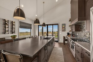 Une cuisine moderne dotée d’un grand îlot central, de luminaires suspendus et offrant une vue sur l’extérieur.