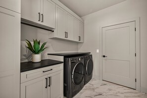 A laundry room with a washing machine, a potted plant, and a white door. - Teton Sunset 3BR luxury home sleeps 12 with private hot tub & unbeatable Teton mtn views. (Driggs)