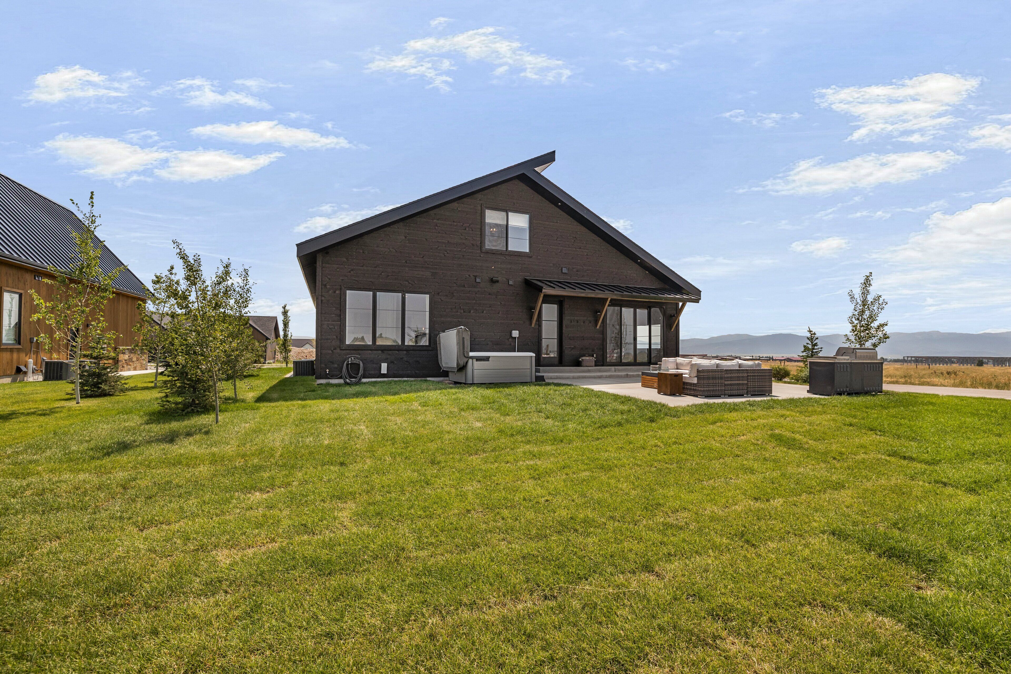 A modern two-story house with a sloped roof, large windows, and a covered patio area.