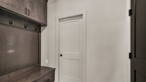 A hallway with a dark wood bench, a white door, and a dark door on the right. - Teton Sunset 3BR luxury home sleeps 12 with private hot tub & unbeatable Teton mtn views. (Driggs)