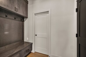A hallway with a dark wood bench, a white door, and a dark door on the right. - Teton Sunset 3BR luxury home sleeps 12 with private hot tub & unbeatable Teton mtn views. (Driggs)