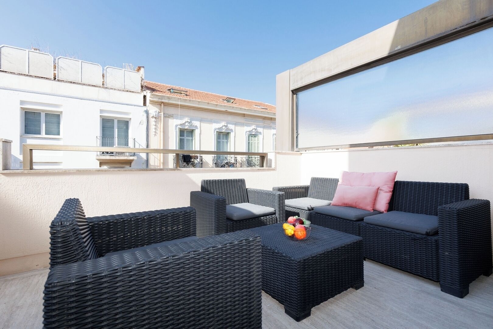Eine Dachterrasse mit Korbmöbeln, einem Tisch mit Früchten und Blick auf Gebäude.