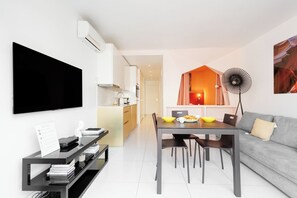 Un espace de vie moderne comprenant un téléviseur à écran plat, une table à manger avec des chaises, un canapé et un coin cuisine à l’arrière-plan.