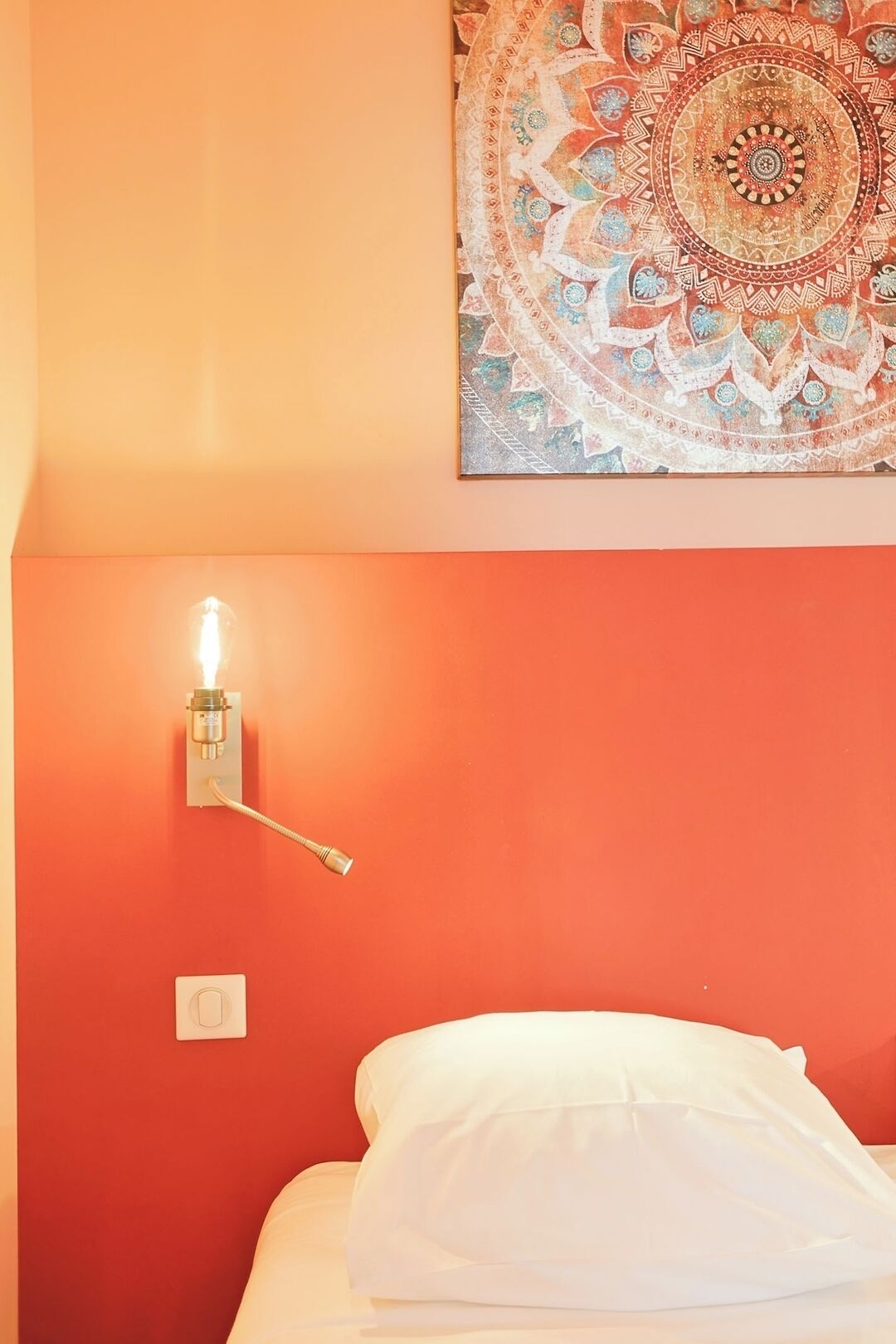 A room with a bed, a wall-mounted light fixture, and a tapestry.