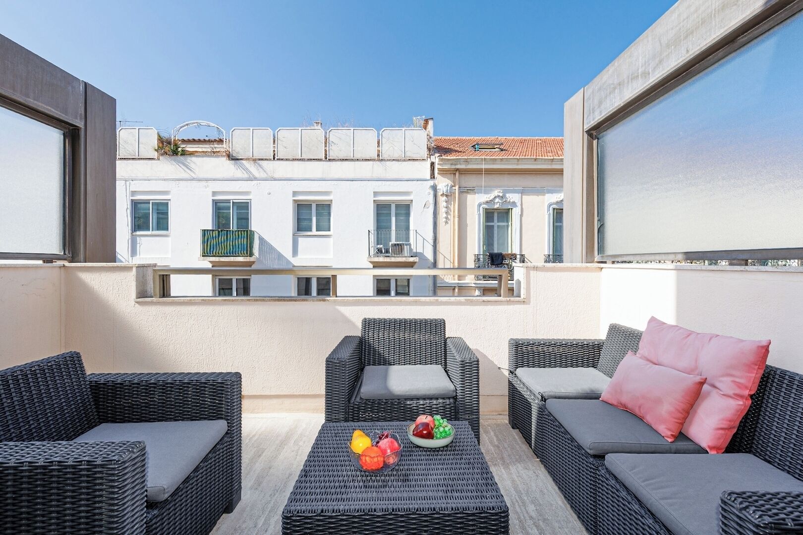 A balcony with wicker furniture, a fruit bowl, and a view of buildings.