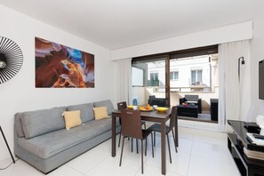 Un salon moderne avec un canapé gris, une table à manger et des chaises. Un grand tableau abstrait orne le mur.