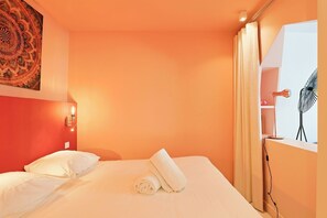 A hotel room with a bed, a wall-mounted artwork, a bedside lamp, a window with curtains, and a fan. - Upstays Elegant Gray d'Albion 2min Palais (Cannes)