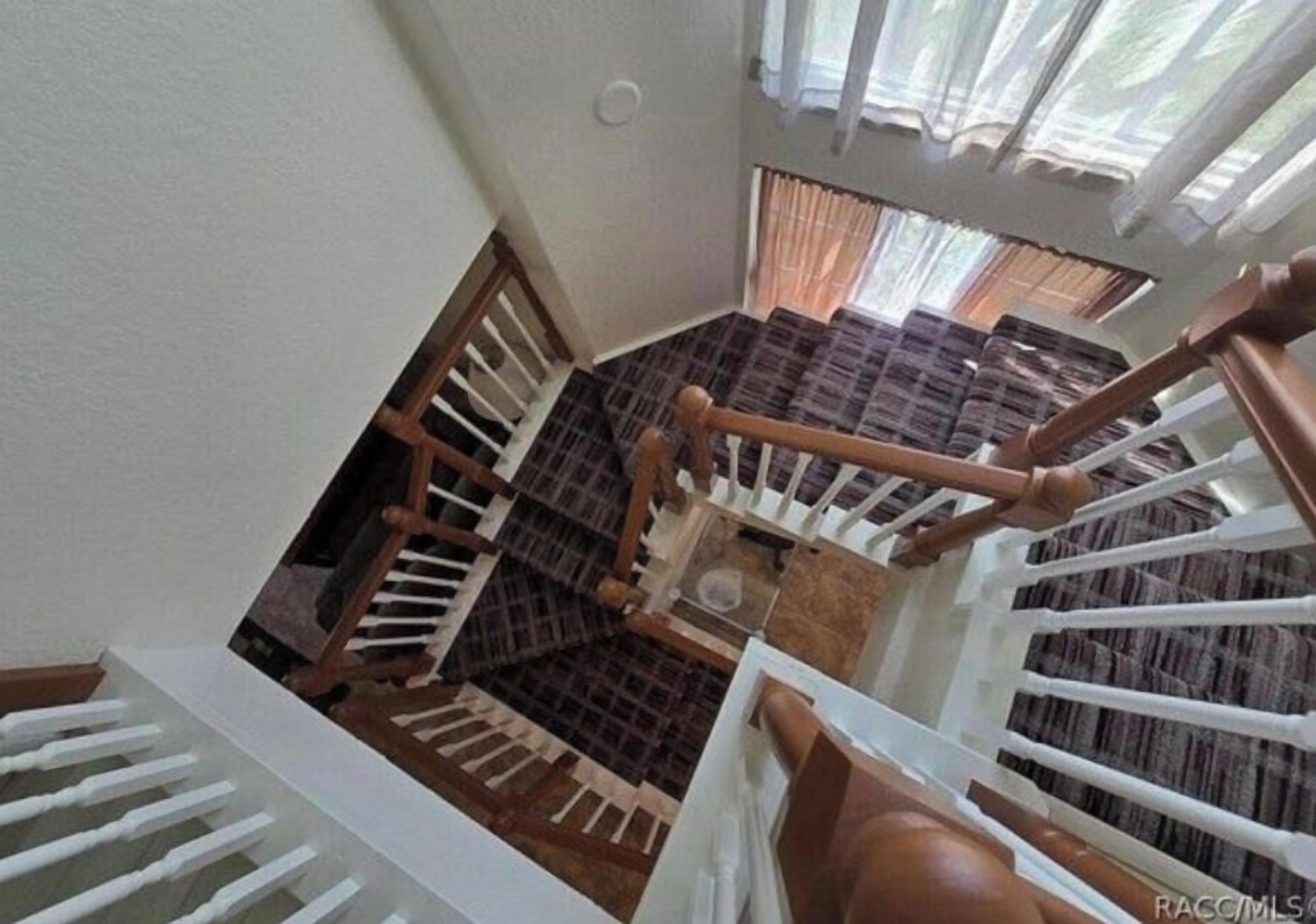 A multi-level interior with a wooden staircase, white railings, and a view of a room with patterned curtains.
