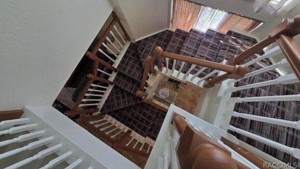 A multi-level interior with a wooden staircase, white railings, and a view of a room with patterned curtains.