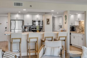 A modern kitchen with white cabinets, stainless steel appliances, and a bar area with bar stools. - New listing! Updated oceanfront 2/2 with private balcony, heated pool, and garage parking (Ormond Beach)