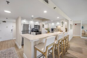 A modern kitchen with a central island, stainless steel appliances, and a seating area with bar stools. - New listing! Updated oceanfront 2/2 with private balcony, heated pool, and garage parking (Ormond Beach)