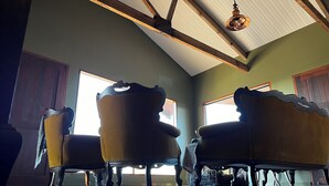 Une pièce dotée d’un plafond haut, de poutres en bois et d’un luminaire suspendu. On y trouve deux fauteuils rembourrés au design incurvé.