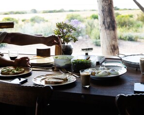 A dining table with various dishes, a cup of coffee, and a view of the outdoors.