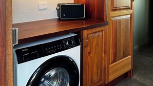 Une petite buanderie équipée d’un lave-linge, d’une radio et de meubles de rangement en bois.