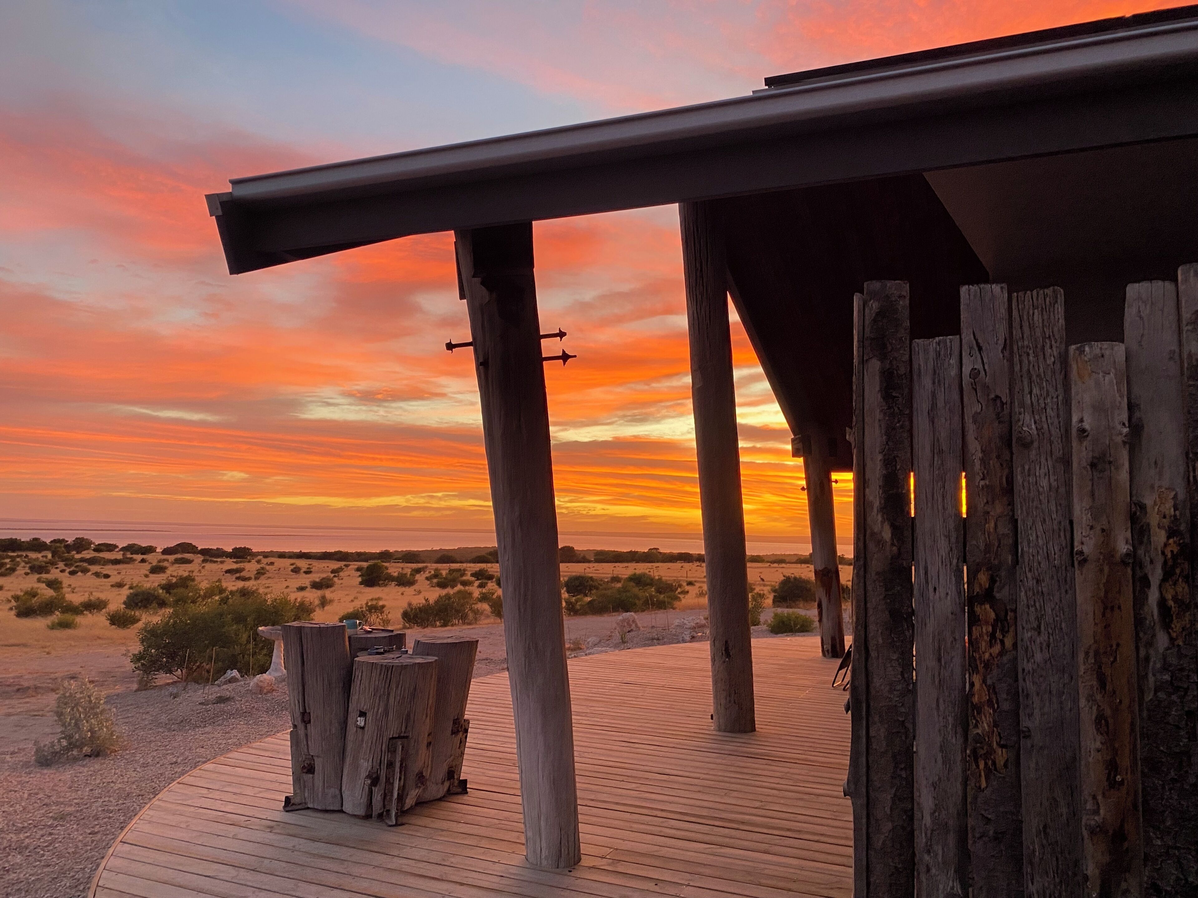 Una terraza de madera con vista a una puesta de sol sobre un paisaje desértico.