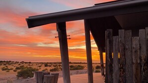 Une terrasse en bois offrant une vue sur un coucher de soleil se déclinant sur un paysage désertique.