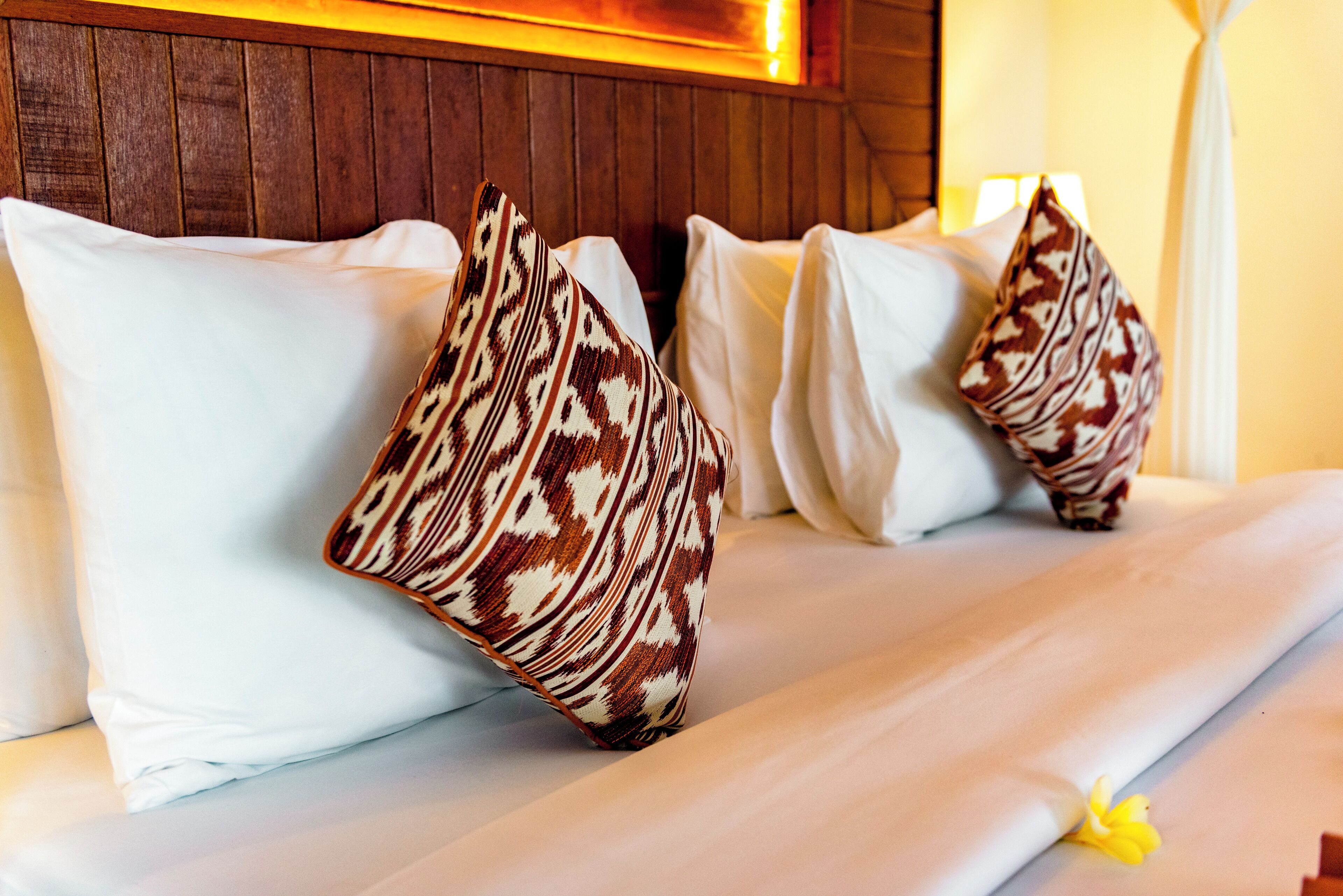 Una cama con almohadas blancas y una manta estampada.