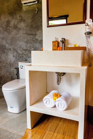 A bathroom with a white toilet, a sink with a soap dispenser, and a towel rack with towels. - Wana Ayu Jelijih Villa (Gianyar)