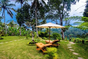 A tropical garden with a lounge area, including a table and two chairs, surrounded by lush greenery and palm trees. - Wana Ayu Jelijih Villa (Gianyar)
