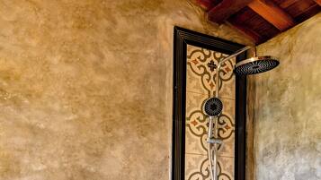 Una doccia con una parete rivestita di piastrelle decorate, uno scaffale in legno con articoli da toilette e un soffitto in legno.