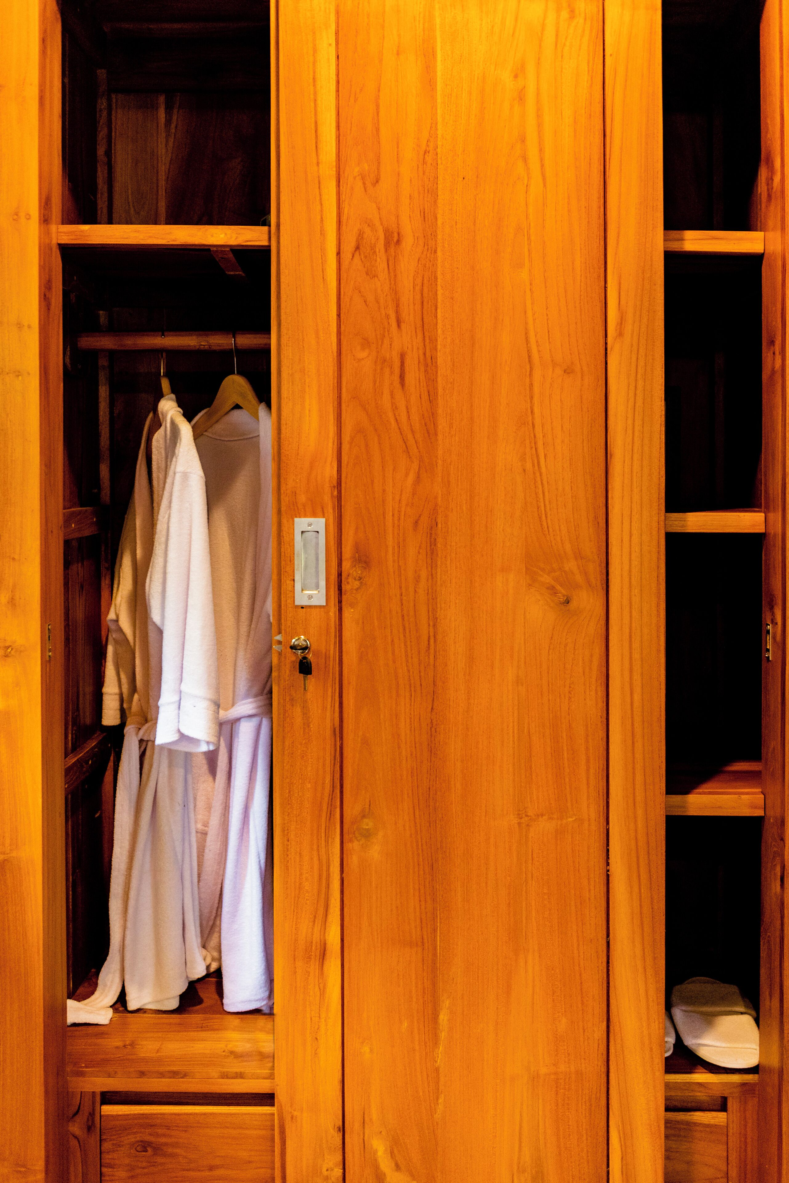 A wooden wardrobe with a hanging rack containing white robes.