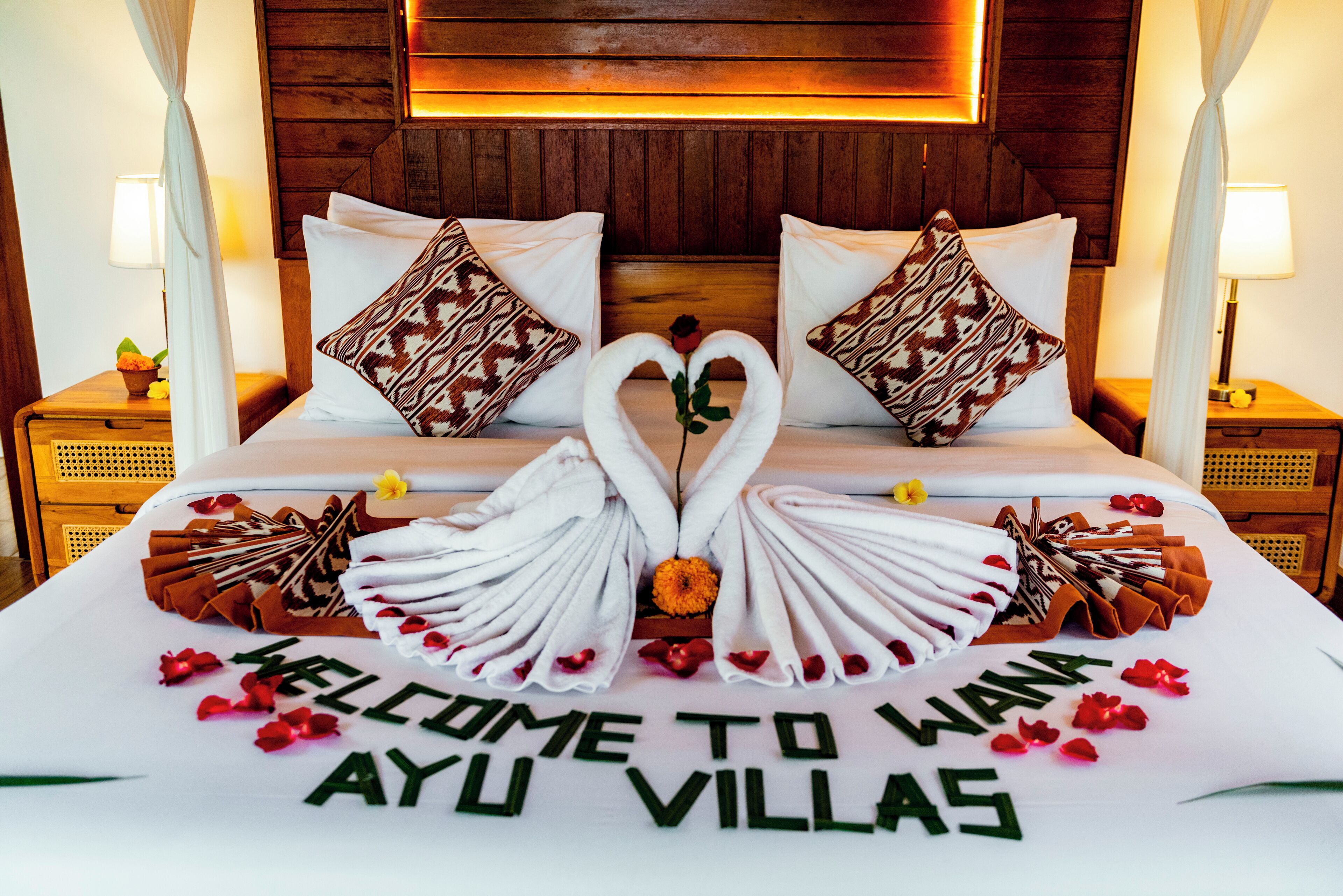A bed with a swan-shaped towel arrangement and a welcome message.
