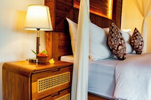 Una cama bien hecha con sábanas blancas, una mesita de noche de madera con una lámpara y almohadones decorativos.
