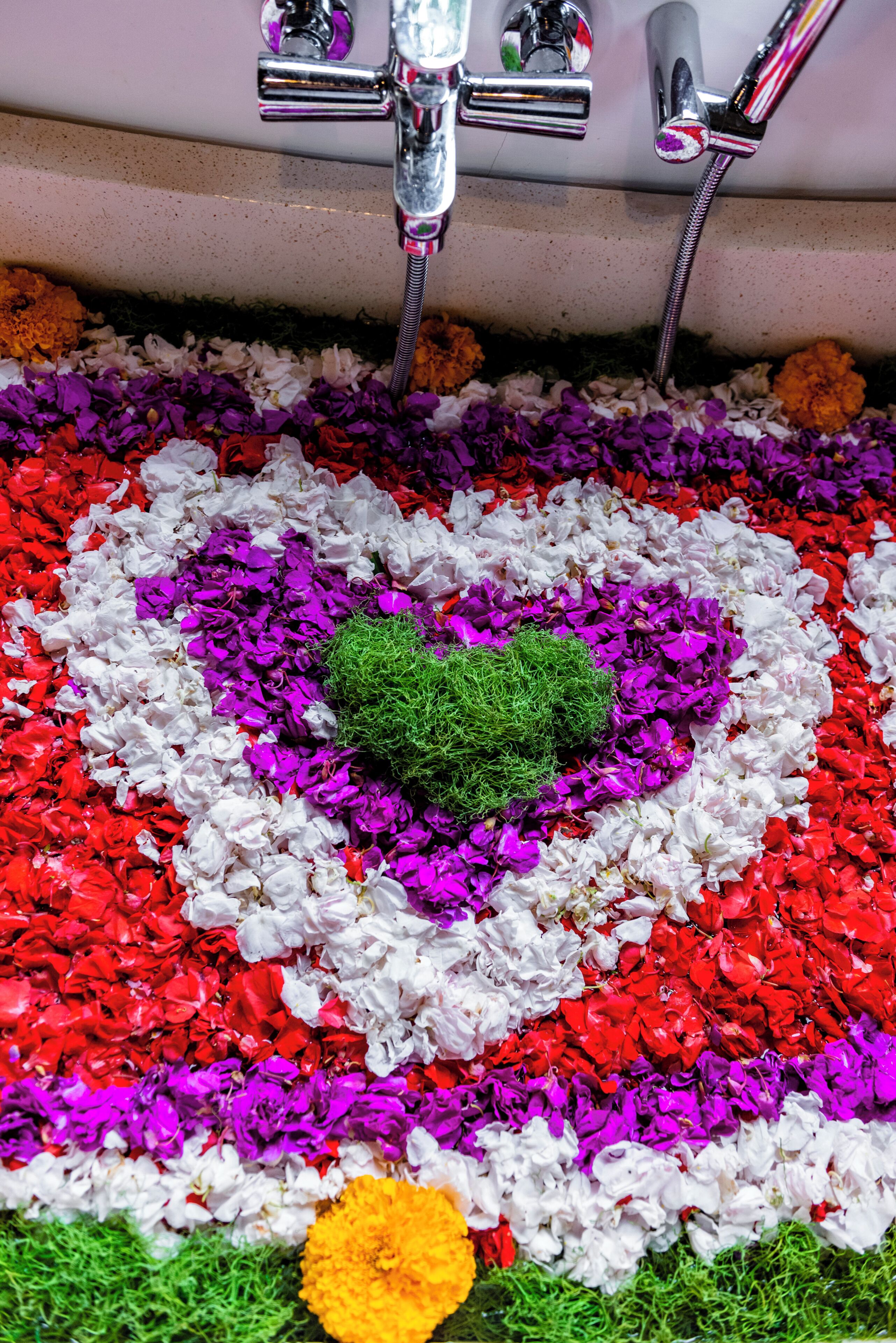 Un baño con un arreglo floral con forma de corazón en el suelo, rodeado de una variedad de pétalos coloridos.