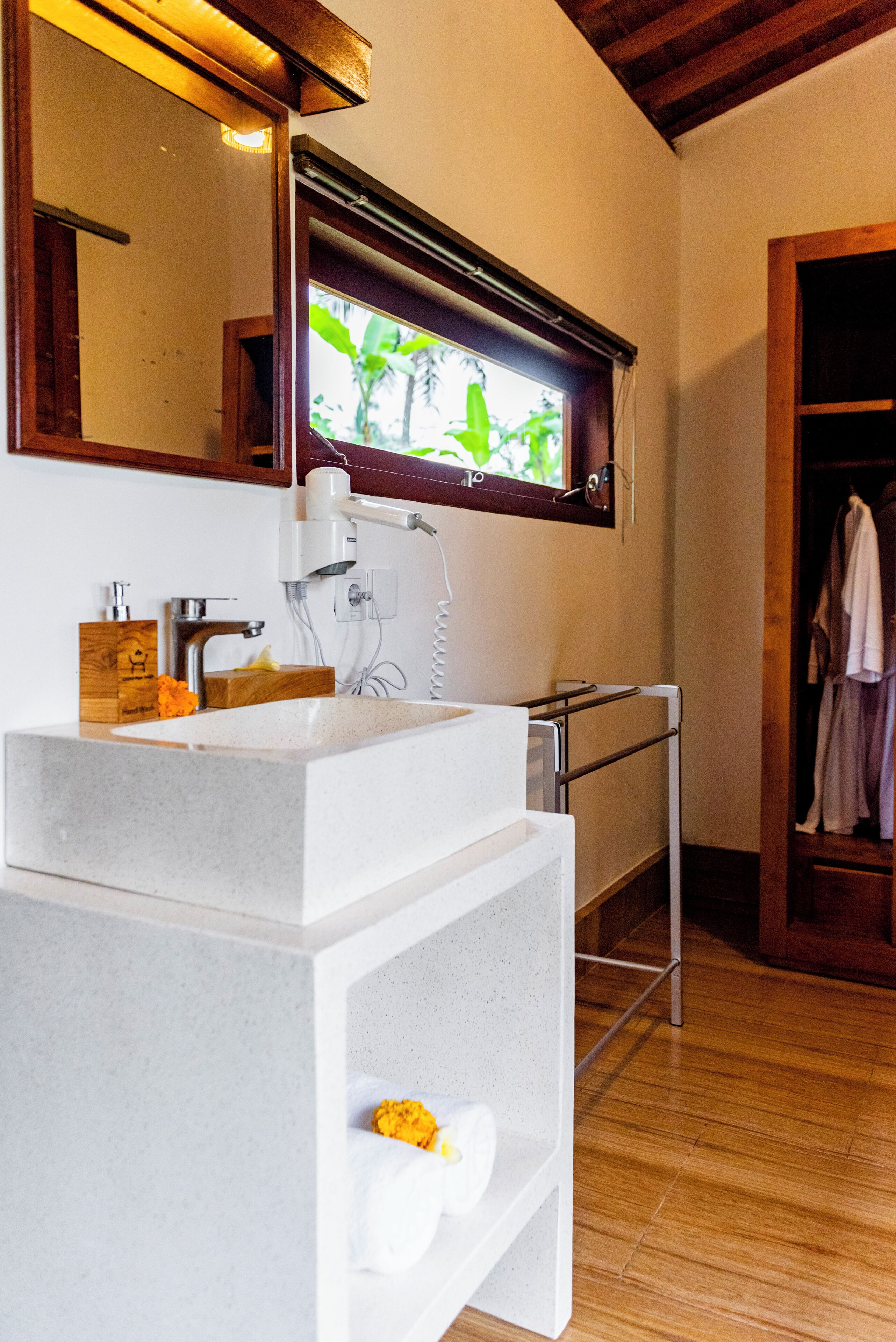A bathroom with a white sink, a mirror, and a window with a view of greenery.